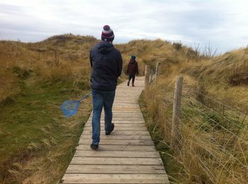 Rear view of man with butterfly net walking on boardwalk