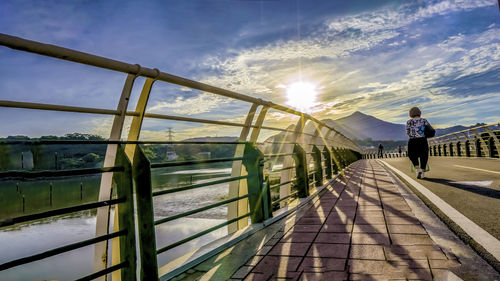 Rear view of woman on footbridge against sky