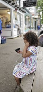 Side view of girl using mobile phone while sitting outdoors