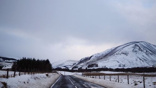 Road by snow covered landscape against sky