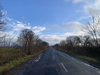 Empty road along bare trees against sky