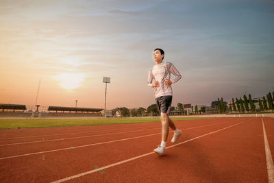 Teenage boy running on sports track against sky during sunset