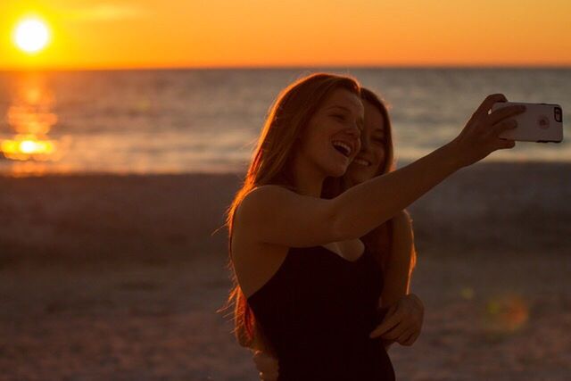 PORTRAIT OF WOMAN PHOTOGRAPHING AT SUNSET