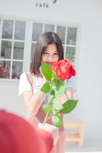 Portrait of smiling woman holding red while standing by potted plant