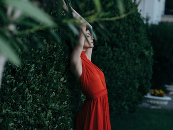 Young woman looking away while standing against plants