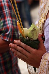 Midsection of woman holding flower buds and incense sticks while praying