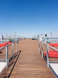 Empty footpath by sea against clear blue sky