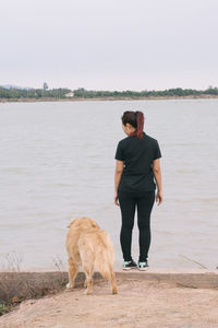 Full length rear view of young woman standing against the sea
