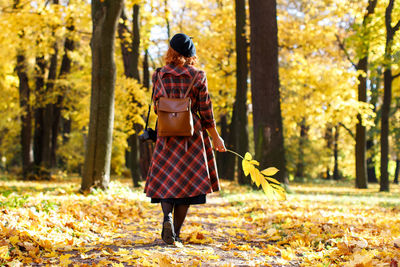 Rear view of woman holding plant standing in forest