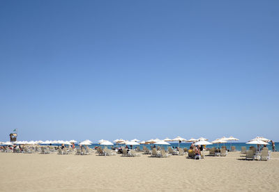 Parasols and lounge chairs at beach against clear blue sky