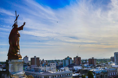 Statue in city against cloudy sky during sunny day