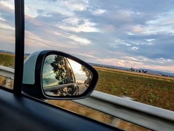 Close-up of side-view mirror against sky