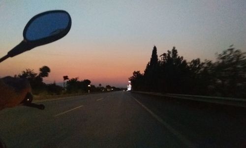 Road by silhouette trees against sky during sunset