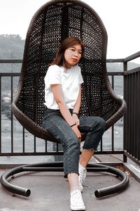 Full length portrait of smiling woman sitting on railing