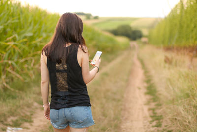 Rear view of woman holding mobile phone on field