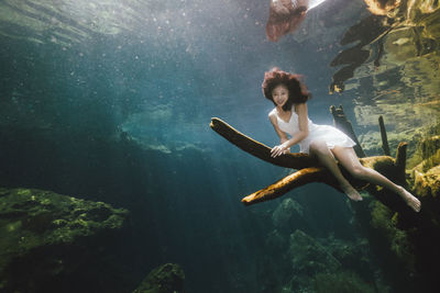 Low angle view of woman sitting on branch underwater