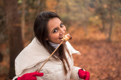 Portrait of young woman eating mushroom while standing at forest