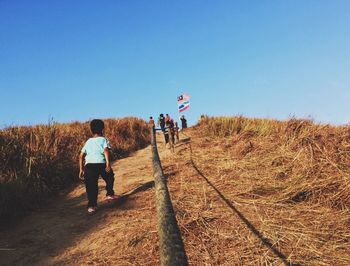 Rear view of people walking on mountain against clear sky