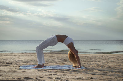 Side view of woman standing at beach against sky