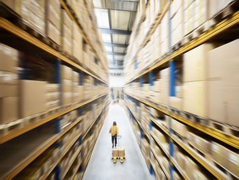 Warehouse worker pulling pallet jack walking in alley amidst racks