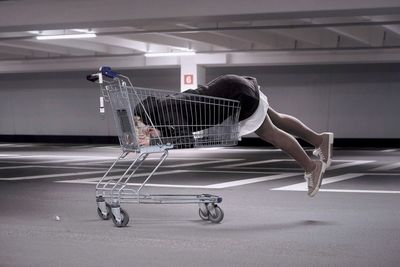 Side view of woman lying in shopping cart at parking garage