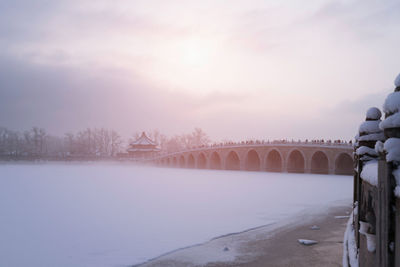 View of bridge on snow covered landscape during sunset