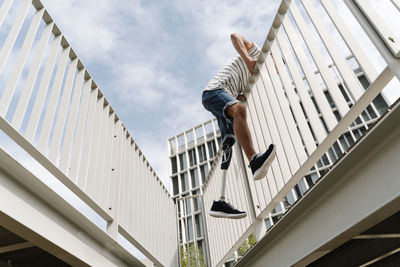 Low angle view of amputed man crossing bridge railing against cloudy sky in city