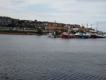 Sailboats in sea by buildings in city against sky