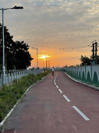 Road by trees against sky during sunset