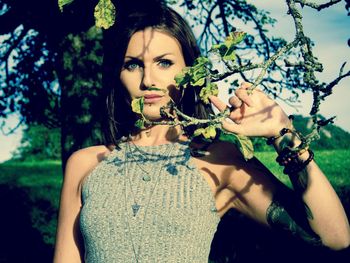 Portrait of beautiful woman standing by tree on sunny day