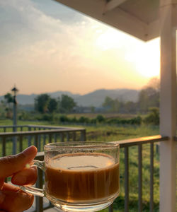 Close-up of hand holding coffee at sunset