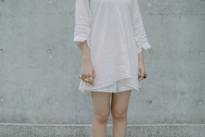 Midsection of young woman wearing rose shape rings against wall