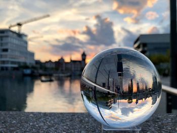 Close-up of crystal ball on water against city during sunset