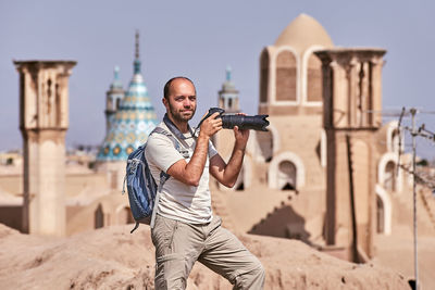 Man holding camera while standing against sky