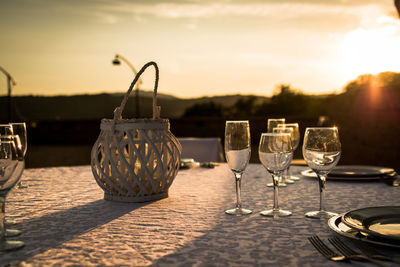 Close-up of wine glasses on table against sea during sunset