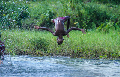 Shirtless boy backflipping over river in forest