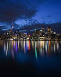 Illuminated buildings by sea against sky at night