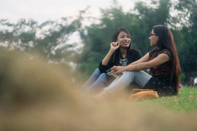 Smiling friends sitting on field against sky