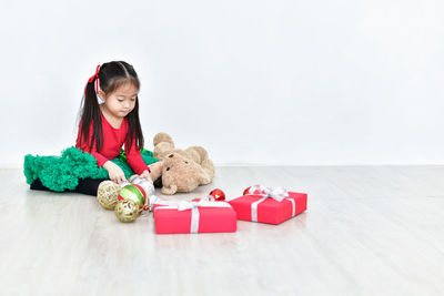 Cute girl sitting with teddy bear and gift boxes on floor during christmas at home