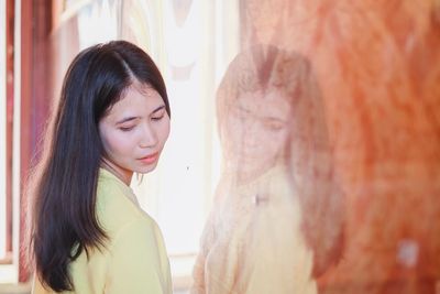 Young woman looking down while standing by window