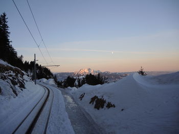 Snow covered road amidst snowcapped mountains against sky during sunset
