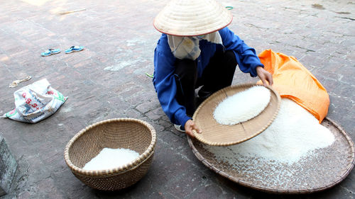Person holding raw rice in wicker plate while crouching on street