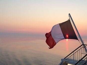 Flag by sea against sky during sunset