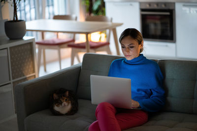 Concentrated woman look at computer pondering ideas, studying at home sitting on couch sofa with pet