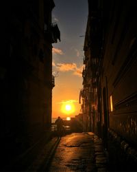 Street amidst silhouette buildings against sky during sunset