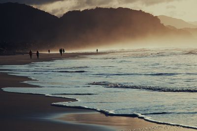 Silhouette people on beach against sky during sunset