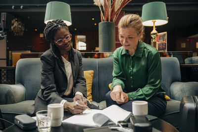 Young businesswoman talking with female colleague while signing contract in hotel lounge