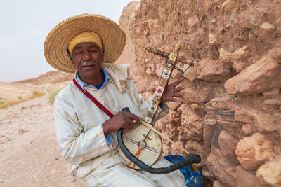 Portrait of man wearing hat standing against stone wall