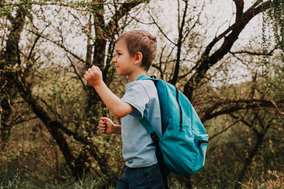 Side view of boy standing by tree