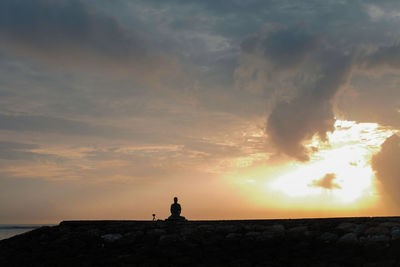 Silhouette rocks by sea against sky during sunset